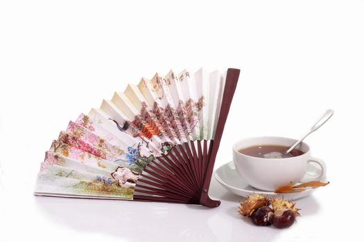 A cup of tea with fan and chestnuts on bright background