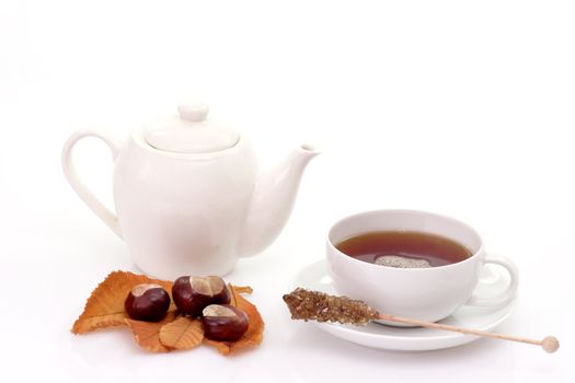 Cup of tea and teapot with autumn foliage on bright background