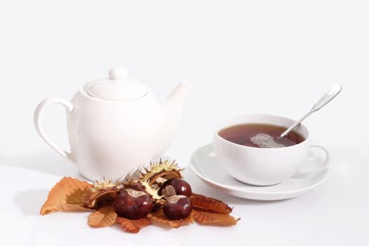 A cup of tea and a teapot with autumn foliage on bright background