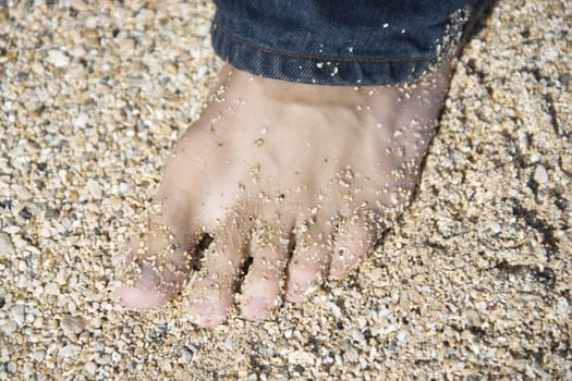 Close up of mid-adult Caucasian male foot wearing jeans on sandy beach.