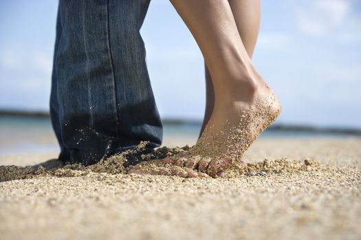 Feet and legs of mid-adult Caucasian couple standing together on beach.