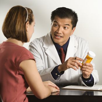 Asian American male doctor explaining medication to Caucasian female patient.