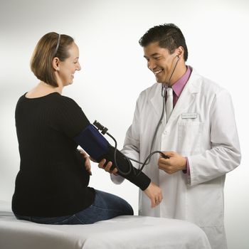Asian American male doctor testing blood pressure of pregnant Caucasian woman.