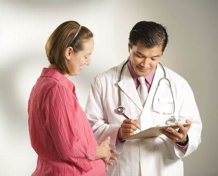 Asian American male doctor consulting with pregnant Caucasian woman.