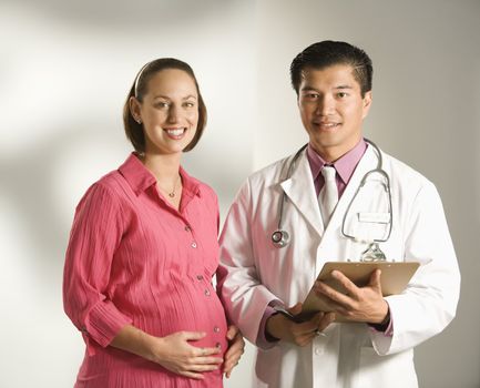 Asian American male doctor consulting with pregnant Caucasian woman.