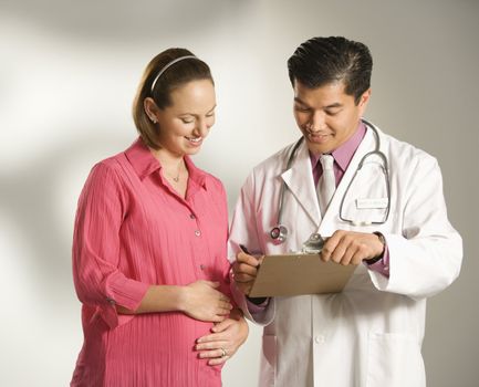 Asian American male doctor consulting with pregnant Caucasian woman.