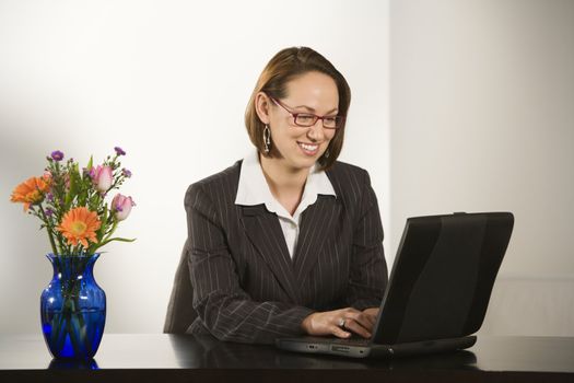 Caucasian businesswoman sitting at desk smiling with laptop computer.