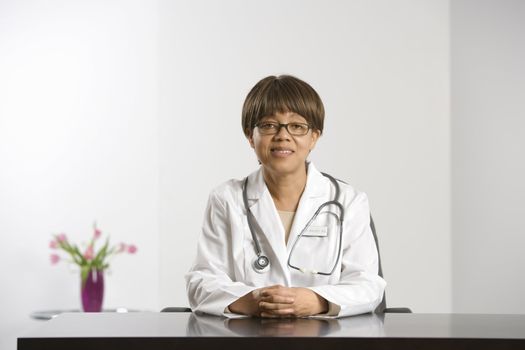 African American middle-aged female doctor sitting at desk smiling and looking at viewer.