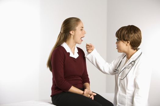 African American middle-aged female doctor examining Caucasian mid-adult female patient with tongue depressor.