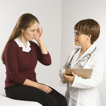 African American middle-aged female doctor listening to Caucasian mid-adult female patient explain her symptoms.