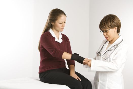 African American middle-aged female doctor examining wrist of Caucasian mid-adult female patient.