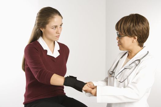 African American middle-aged female doctor examining wrist of Caucasian mid-adult female patient.