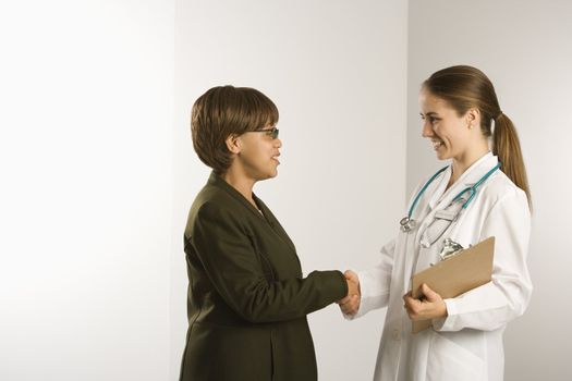 Caucasian mid-adult female doctor shaking hands with African American middle-aged female patient.