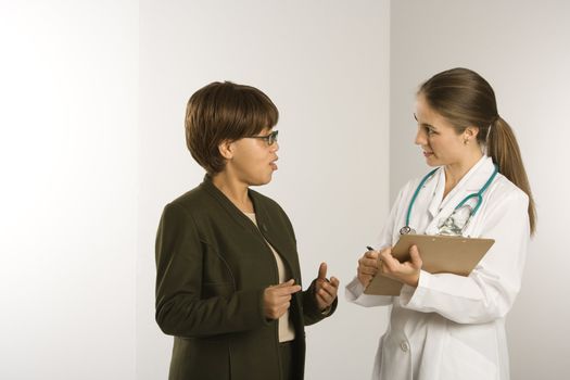 Caucasian mid-adult female doctor talking with African American middle-aged female patient.