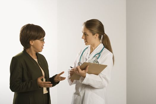 Caucasian mid-adult female doctor talking with African American middle-aged female patient.
