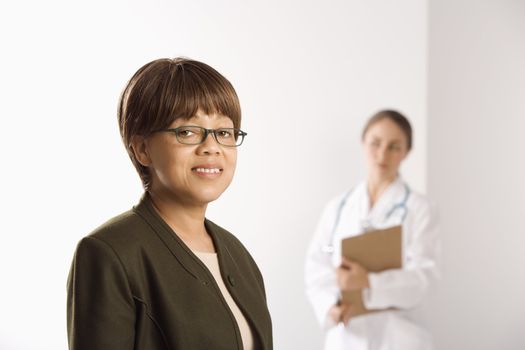 African American middle-aged female patient woman smiling looking at viewer with Caucasian mid-adult female doctor standing in background.