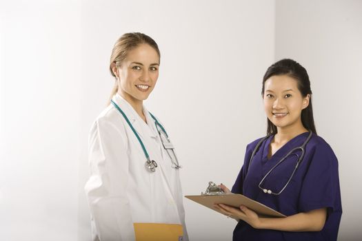Caucasian mid-adult female doctor and Asian Chinese mid-adult female physician's assistant standing together smiling and looking at viewer.