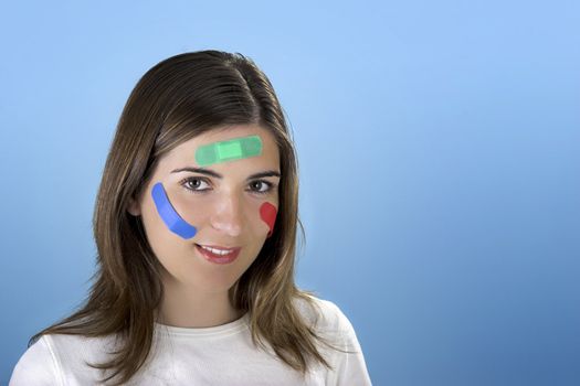 Beautiful woman with colored bandages on the face over a blue background