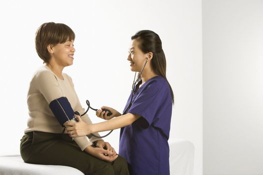 Asian Chinese mid-adult female medical practitioner checking blood pressure of African American middle-aged female patient.