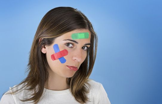 Beautiful woman with colored bandages on the face over a blue background