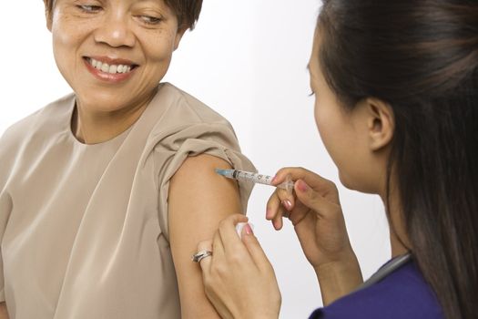 Asian Chinese mid-adult female medical practitioner giving shot in arm of African American middle-aged female patient.