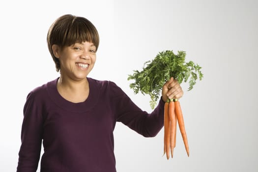 Portrait of African American middle-aged woman holding bunch of fresh carrots smiling and looking at viewer.