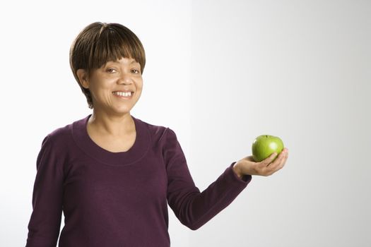 Portrait of African American middle-aged woman holding green apple smiling and looking at viewer.