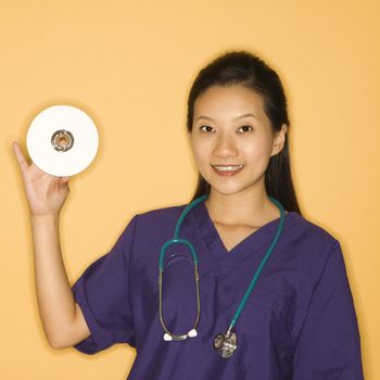 Asian Chinese mid-adult female doctor holding holding up CD against yellow background smiling and looking at viewer.