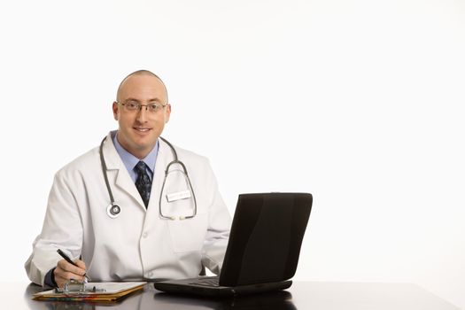 Caucasian mid adult male physician sitting at desk with laptop computer.