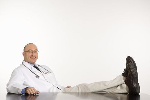 Caucasian mid adult male physician sitting with feet on desk smiling.