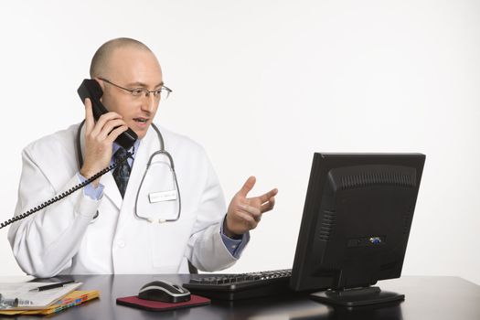 Caucasian mid adult male physician sitting at desk with laptop computer talking on telephone.
