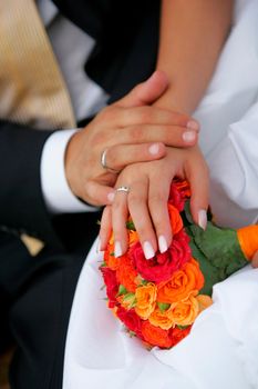 Close up of loving newlywed couple holding hands over red bouquet of flowers.
