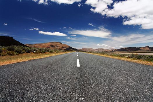 Long, lonely road in front of blue sky and mountains