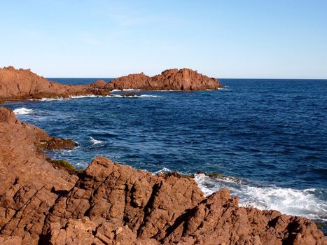 Red rocks and blue mediterranean sea with waves at the Esterel massif, south of France, by beautiful weather