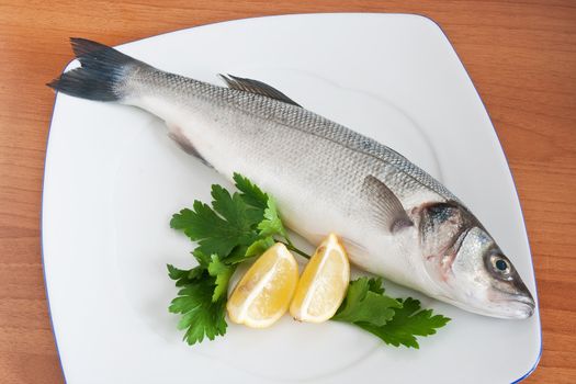 plate with sea bass, lemon and parsley isolated on wooden background