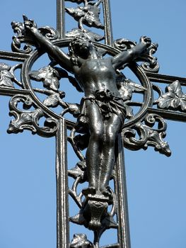 Jesus cross made of black metal with lots of decorations around and blue sky behind