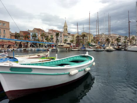 Colored boats, port, buildings and famous bell tower of the church at Sanary-sur-mer, sout of France, by cloudy weather