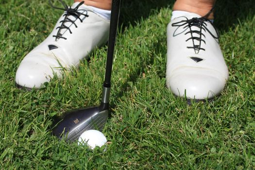 White golf shoes, a golfclub and a golfball