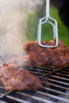 Grilled chuck steak hold in metal tongs. Shallow depth of field.