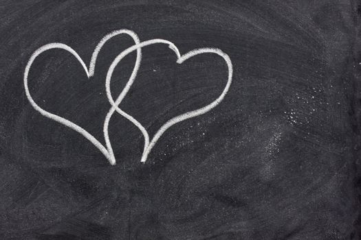 two interlaced hearts sketched with white chalk on a blackboard 