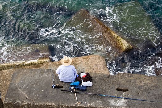 Fisherman in hat is sitting on the stone and fishing, top horizontal view