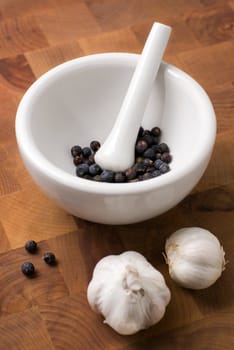 Juniper in ceramic mortar and pestle and garlic on the wood cutting board.