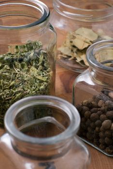 Glass jars with herbs - allspice, dried bay leafs and marjoram or oregano or other green.