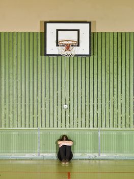 Sad girl sitting under a basket hoop