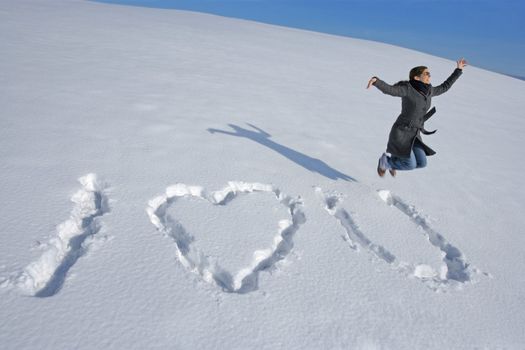 A happy woman jumping after writing I love you in the snow.
