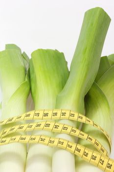Fresh leek with measuring tape on bright background