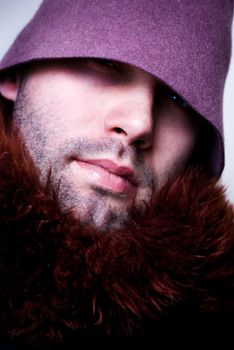 Portrait of young man wearing purple hat and fur, sparkle in the eye, eyes in shadow.