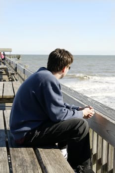 A young man sitting on a pier at the ocean.