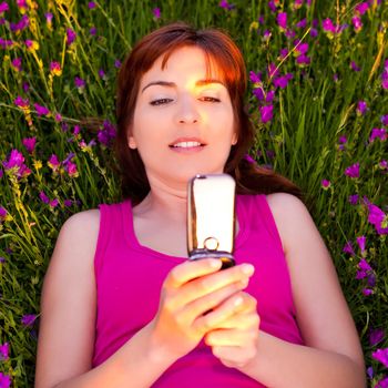 Top view of beautiful young woman lying on the nature and talking at cellphone 