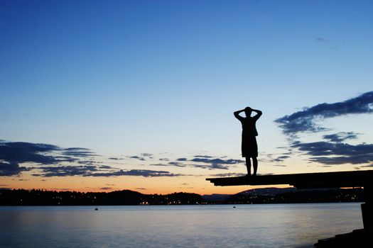 A young person sitting on a dock at dusk, at the fjord in Oslo, Norway